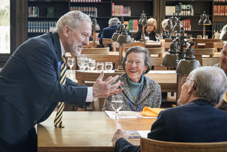 Lyons leans over a table, gesturing, while chatting with seated donors