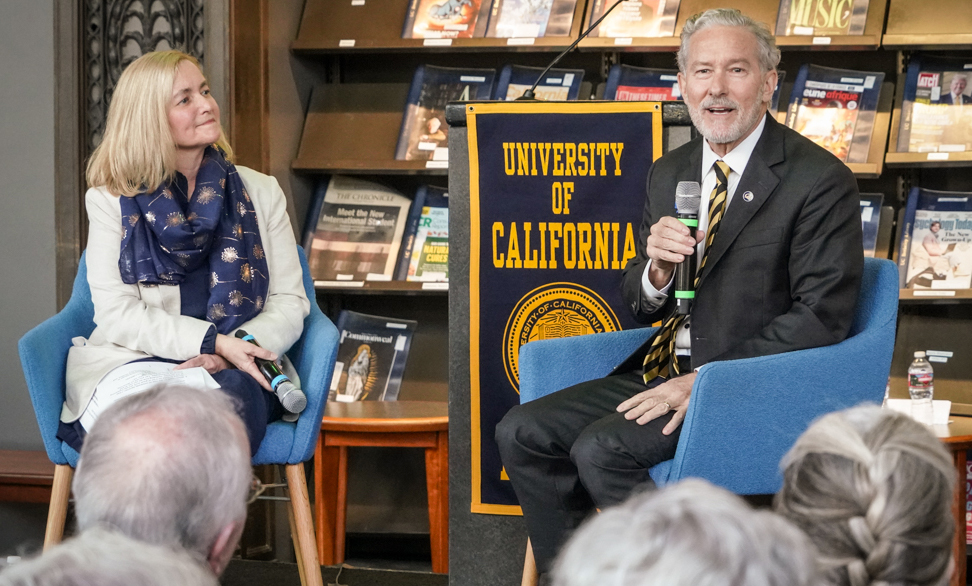 University Librarian and the chancellor sit on a stage with microphones